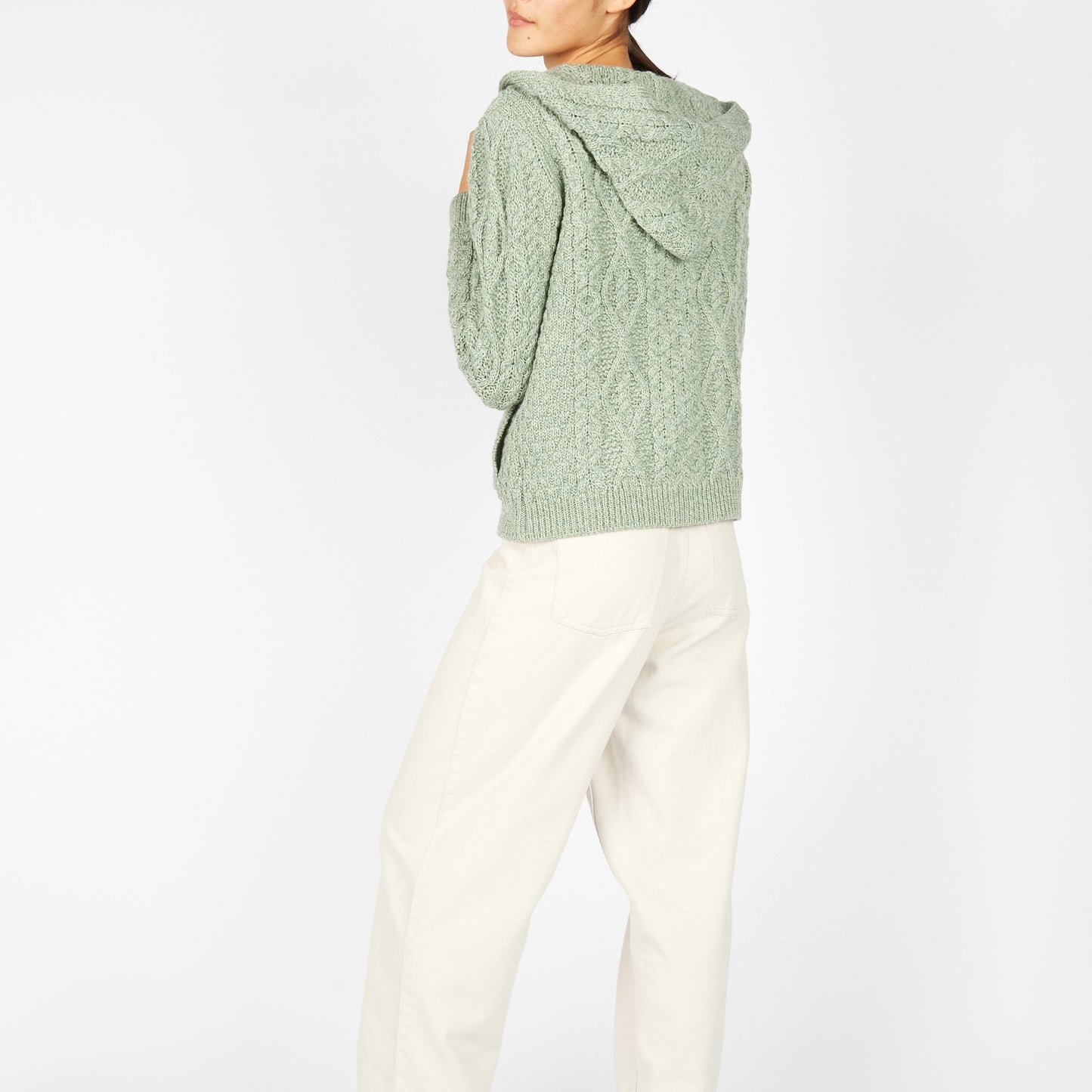 Person wearing a green cable knit sweater and white pants on a white background