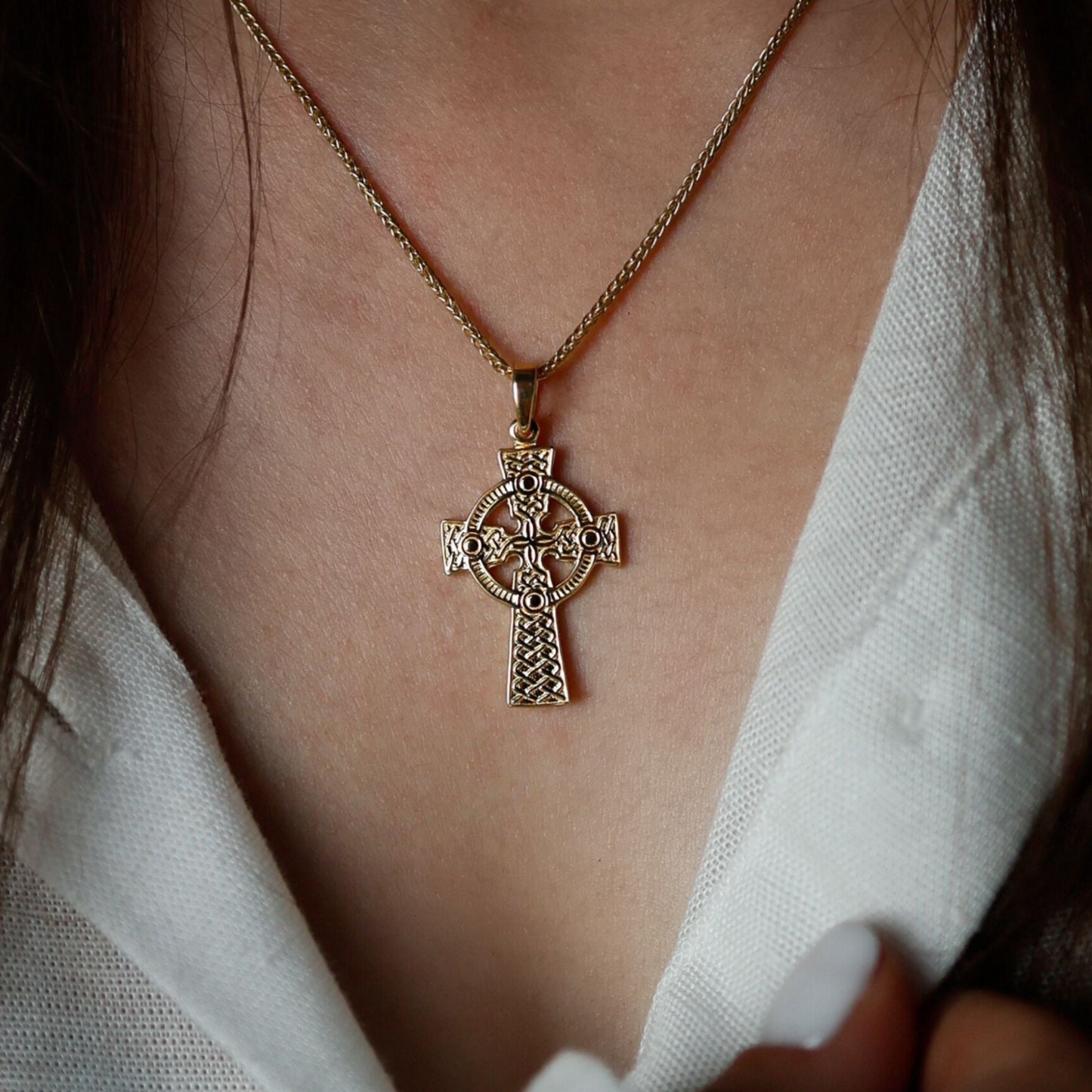 Close-up of a woman wearing a golden Celtic cross pendant on a chain necklace.
