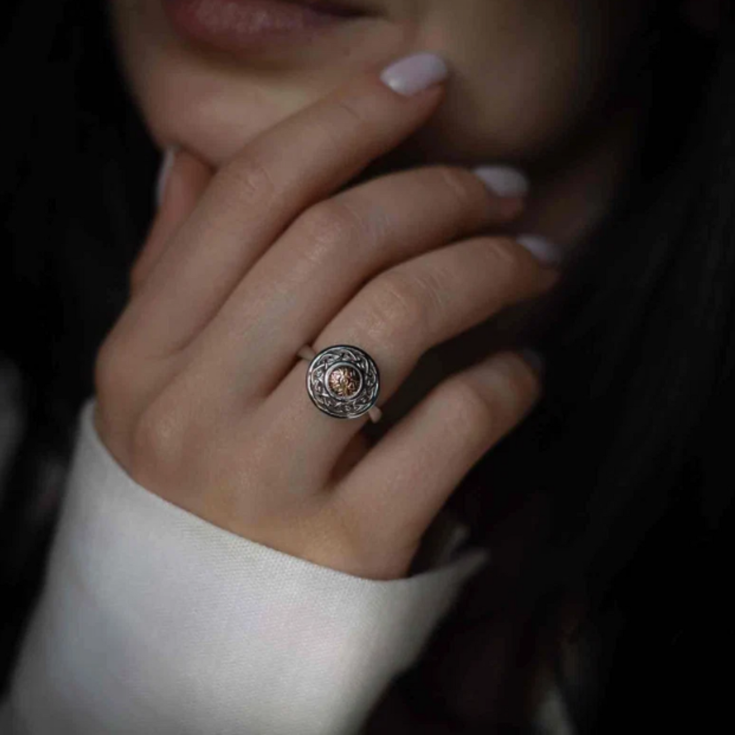 A close-up photo of a woman wearing a shield-shaped silver and gold ring.