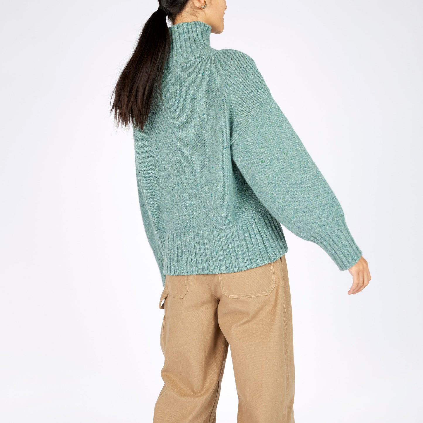 Person wearing a green sweater and beige pants on a white background