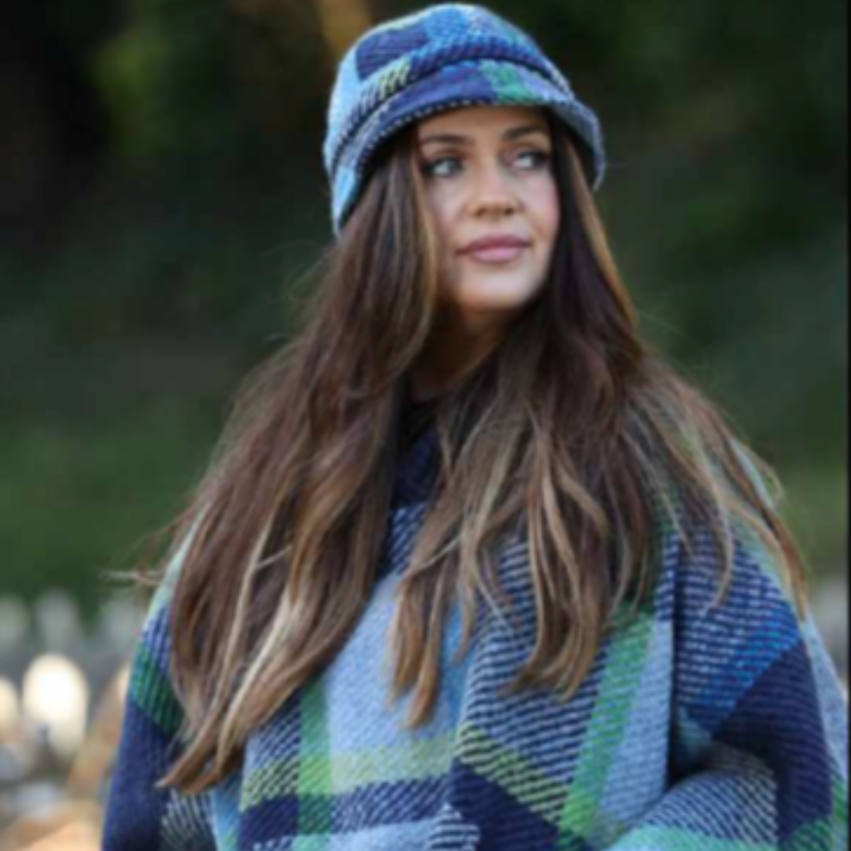 Woman wearing a blue and green plaid poncho and matching hat outdoors.