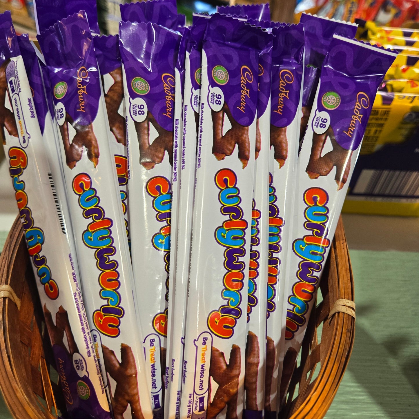 Multiple Cadbury Enthusiast chocolate sticks with purple wrappers standing upright in a woven basket, with a blurred store background.