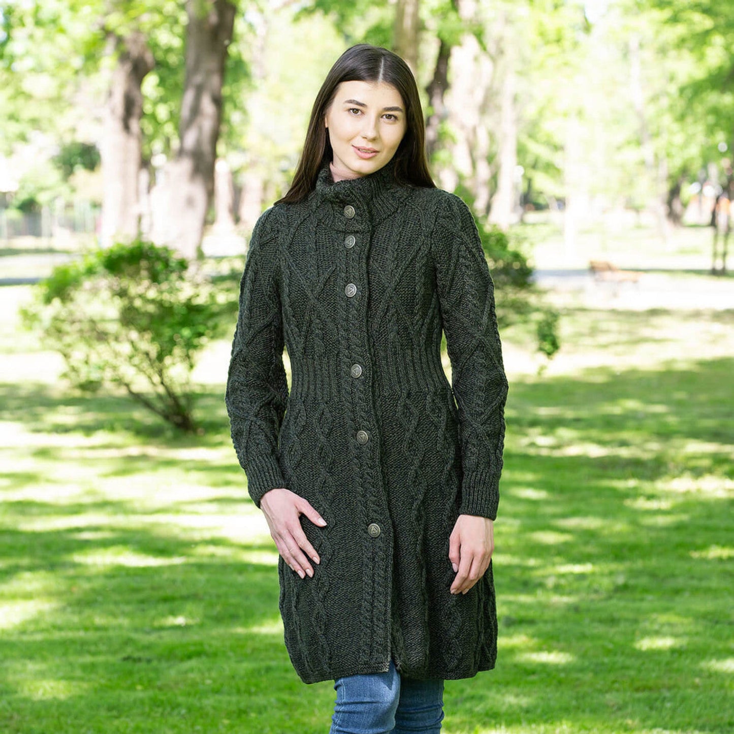 A woman standing in a park wearing a navy Aran Cable Signature Coat with a raised collar and Celtic Knot buttons.