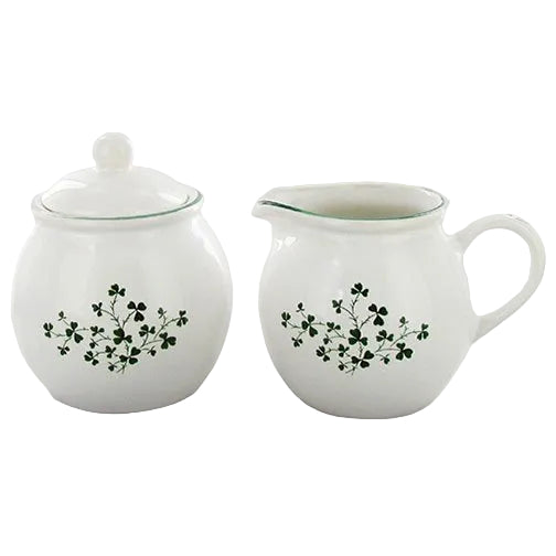 A white ceramic sugar bowl with a lid and a creamer jug, both featuring a green shamrock pattern.