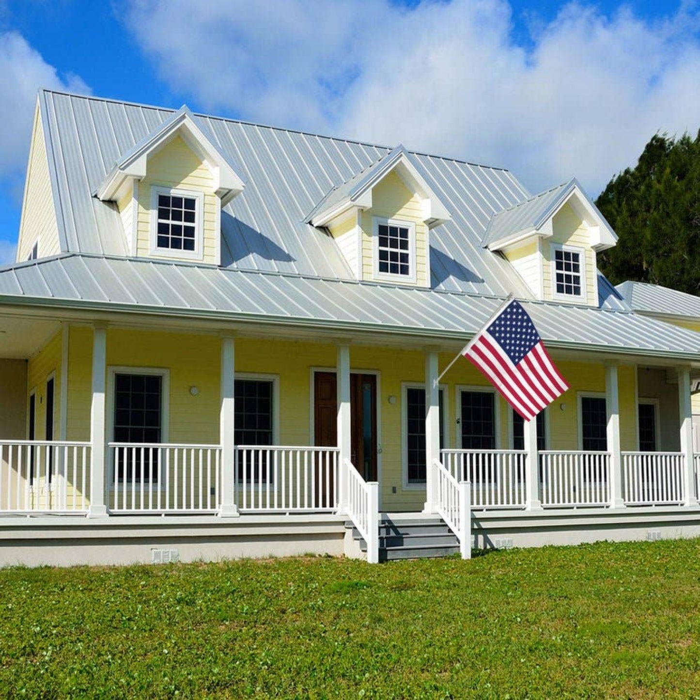 Yellow house with a white porch flying an American flag.