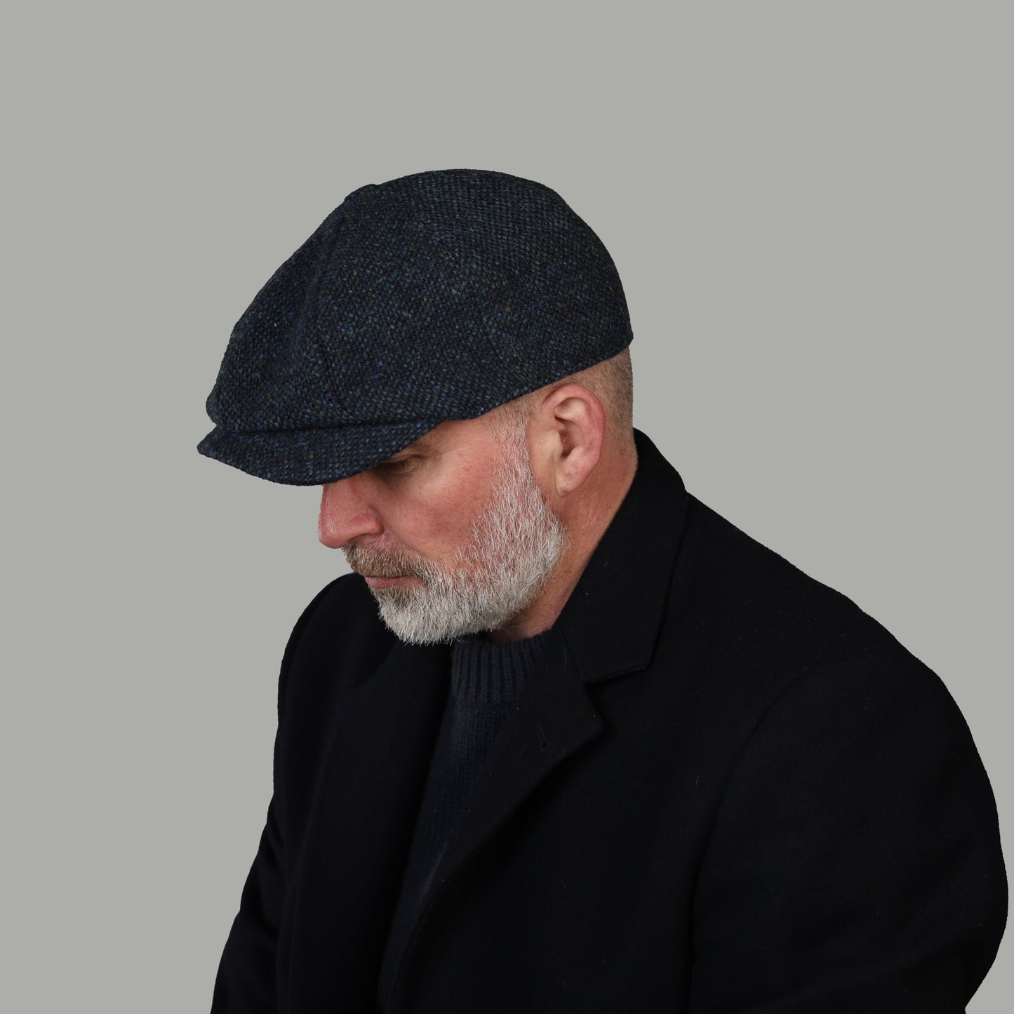 Man wearing a dark textured cap and black coat against a gray background