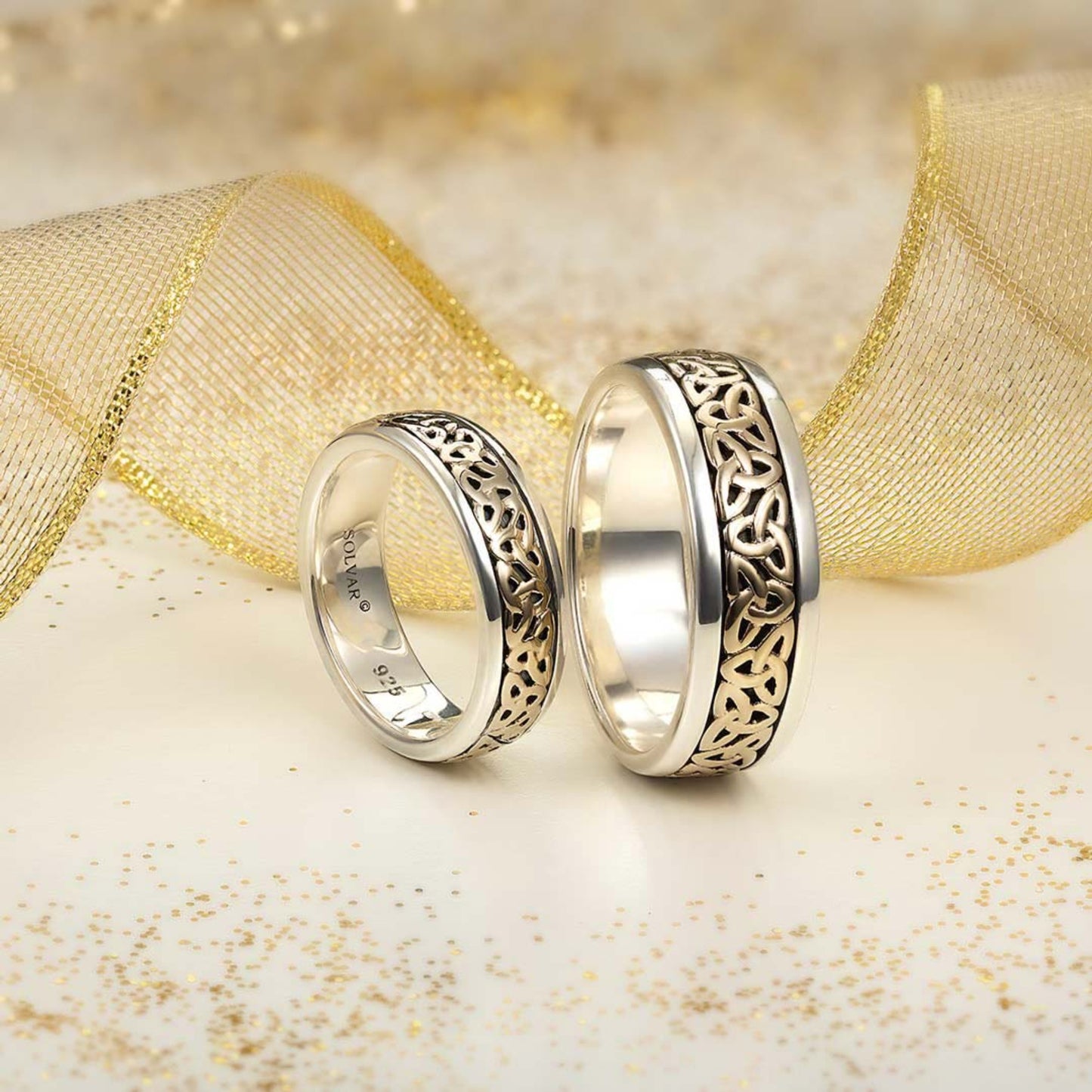 Two silver rings with intricate designs on a gold and white textured background
