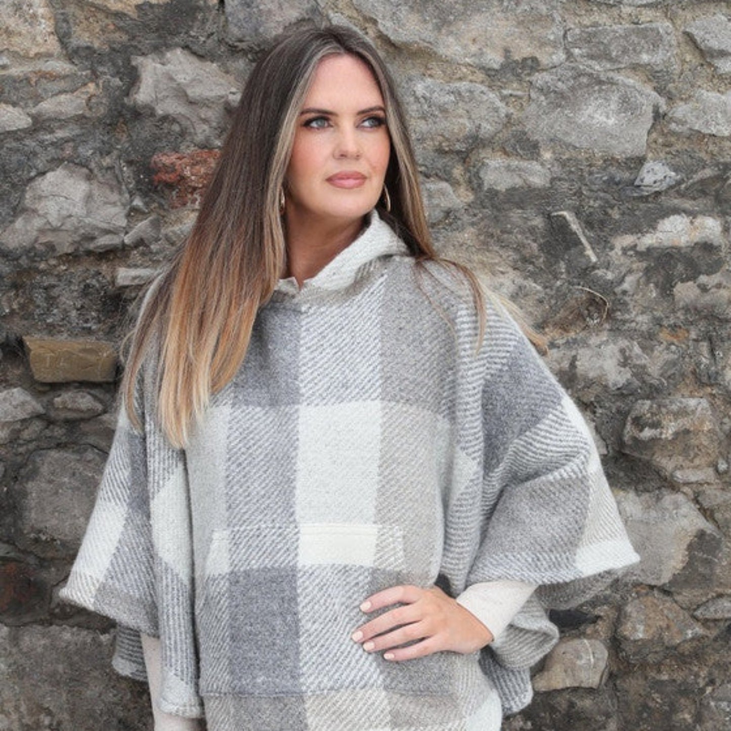 Woman wearing a plaid poncho against a stone wall