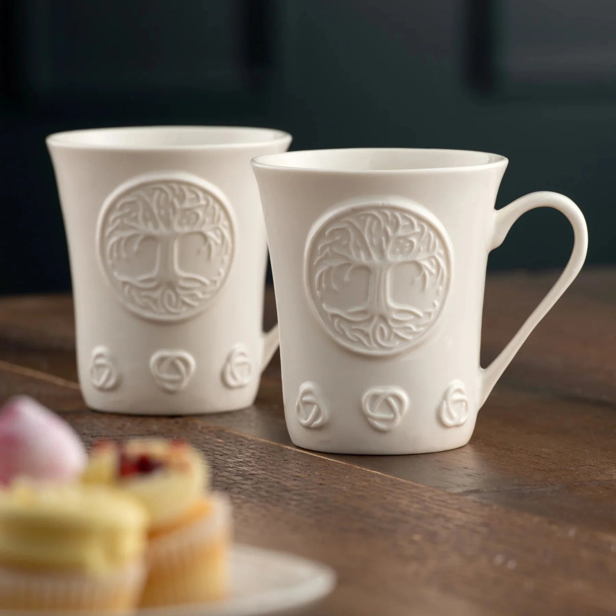 Two white porcelain mugs with tree of life designs on a wooden surface.
