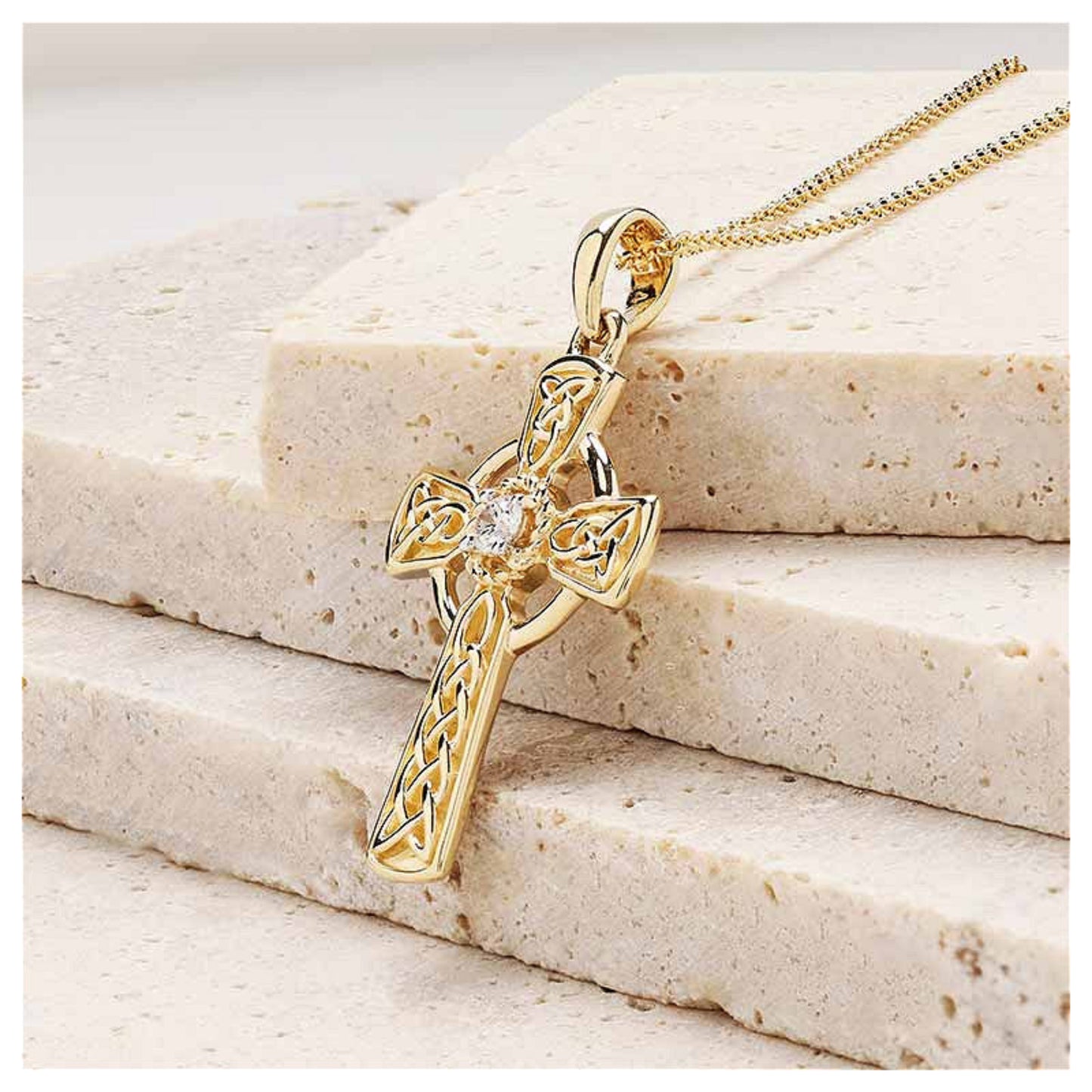 Gold celtic cross pendant sitting on a marble surface