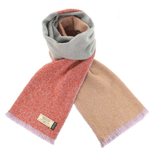 A color block Merino wool scarf in shades of red, orange, and beige, with a label that reads 'Mucros Weavers, Scotland.'