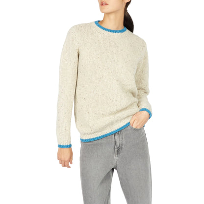 Person wearing a cream sweater with blue trim and gray pants on a white background
