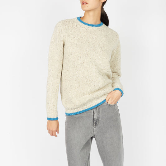 Person wearing a cream sweater with blue trim and gray pants on a white background