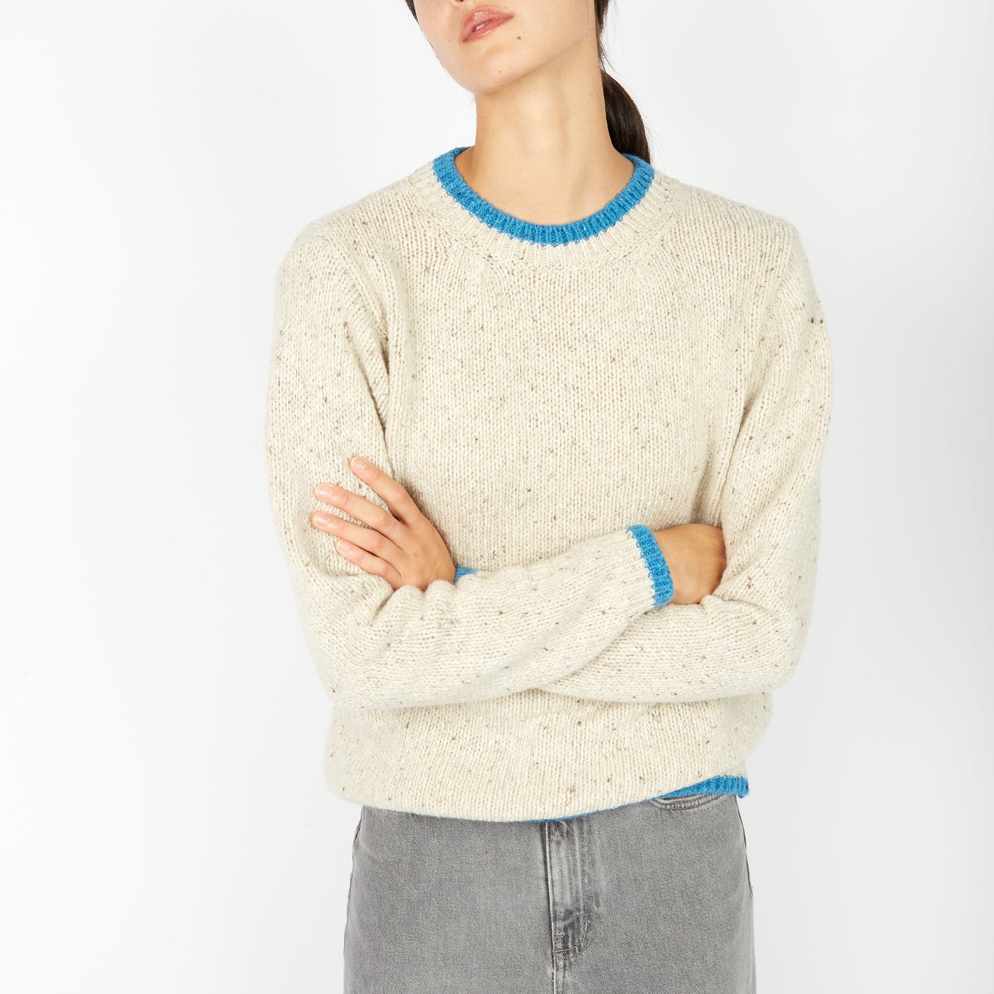 Person wearing a cream sweater with blue trim on a white background
