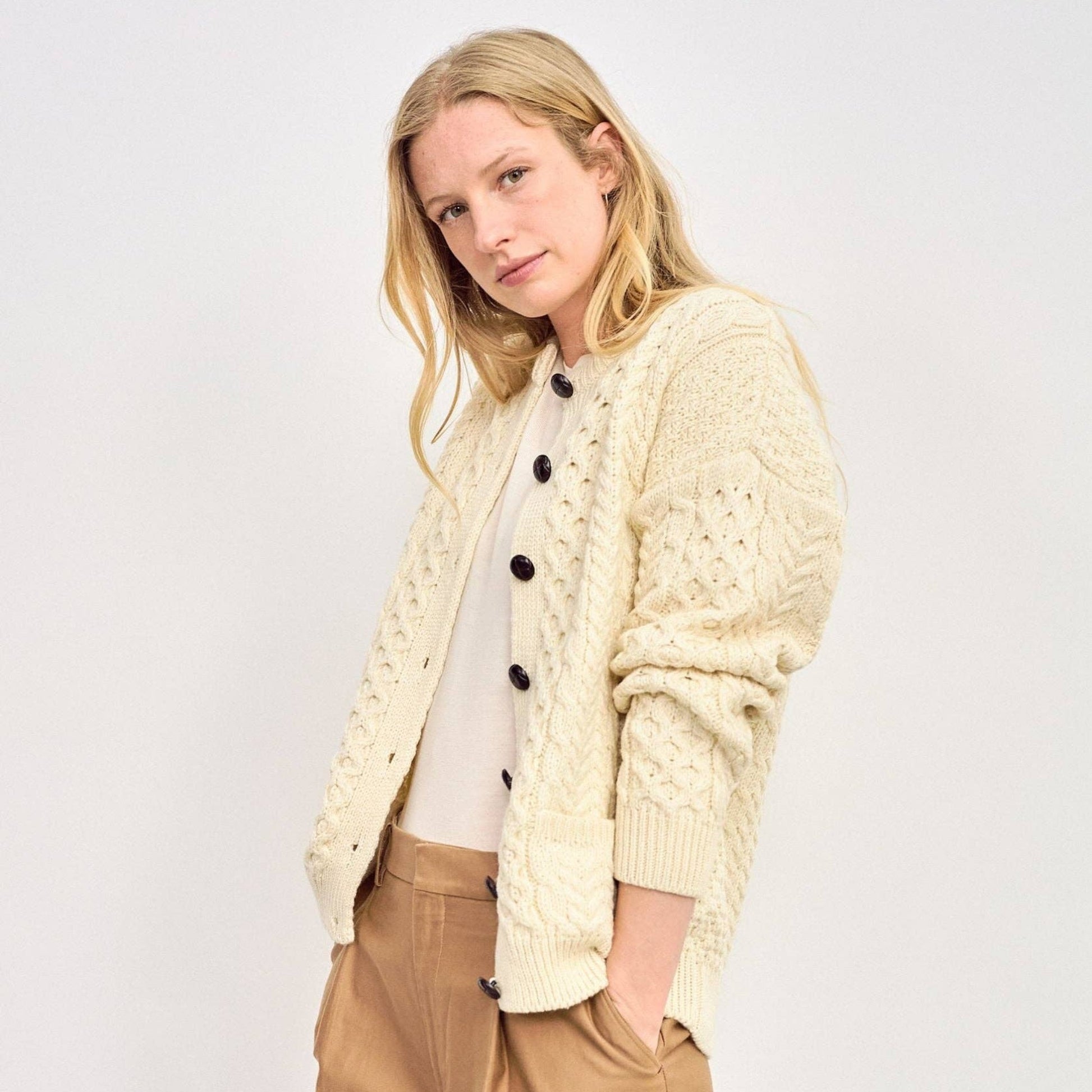 Woman wearing a cream cardigan over a white shirt and beige pants on a white background