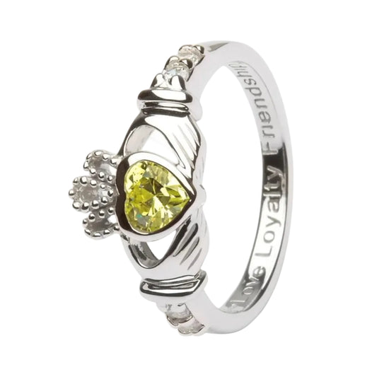 A Claddagh birthstone ring with a green peridot center stone and white metal band, featuring the hands holding a crowned heart symbol.