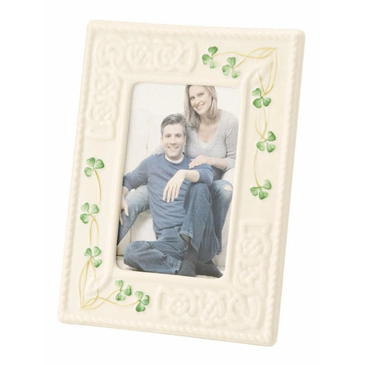 A beige china picture frame with a clover pattern around the border, containing a photo of a couple seated close by the frame's glass.