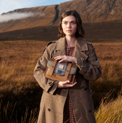 Woman holding a wooden box in a scenic outdoor setting with mountains and grass.