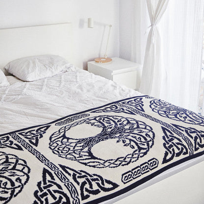 Bed with a decorative blue and white patterned throw blanket in a bright bedroom.