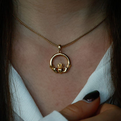 Close-up of a woman wearing a golden necklace with a circular claddagh pendant. 