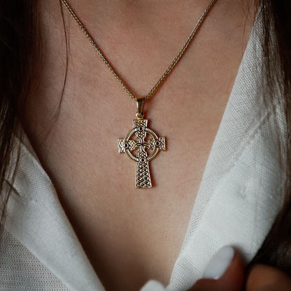 Close-up of a woman wearing a  golden Celtic cross pendant on a chain necklace.
