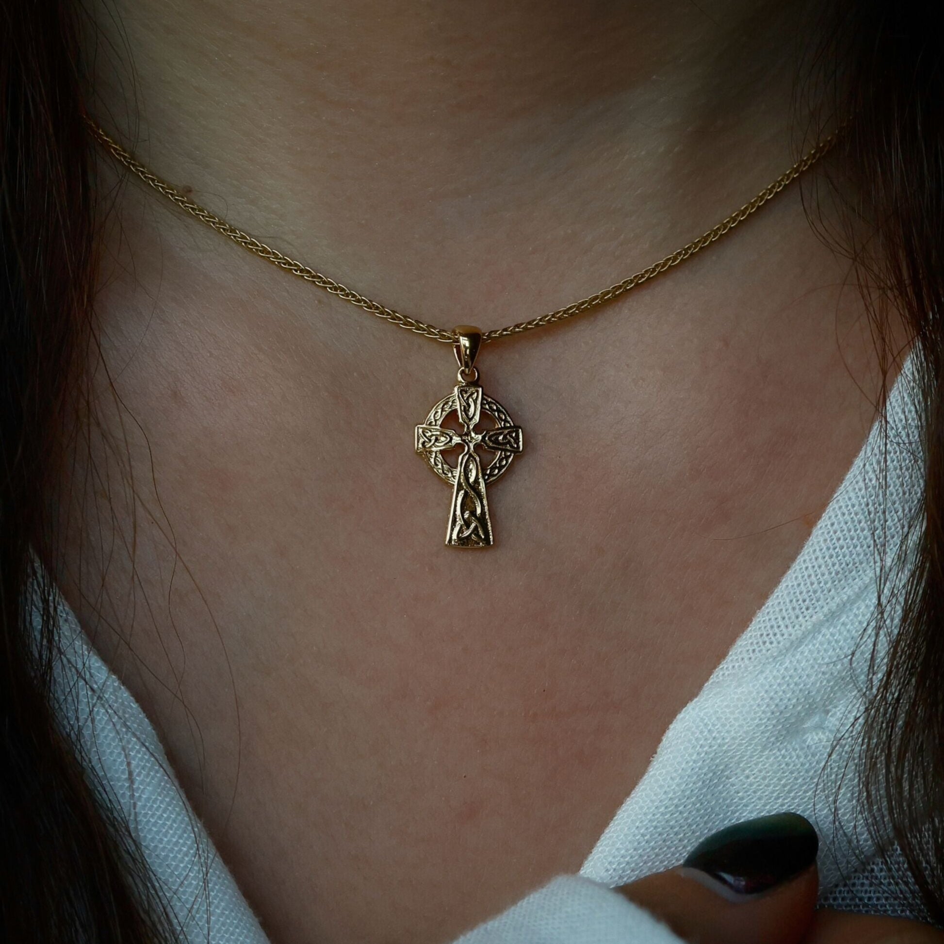 Close-up of a woman wearing a golden Celtic cross necklace.