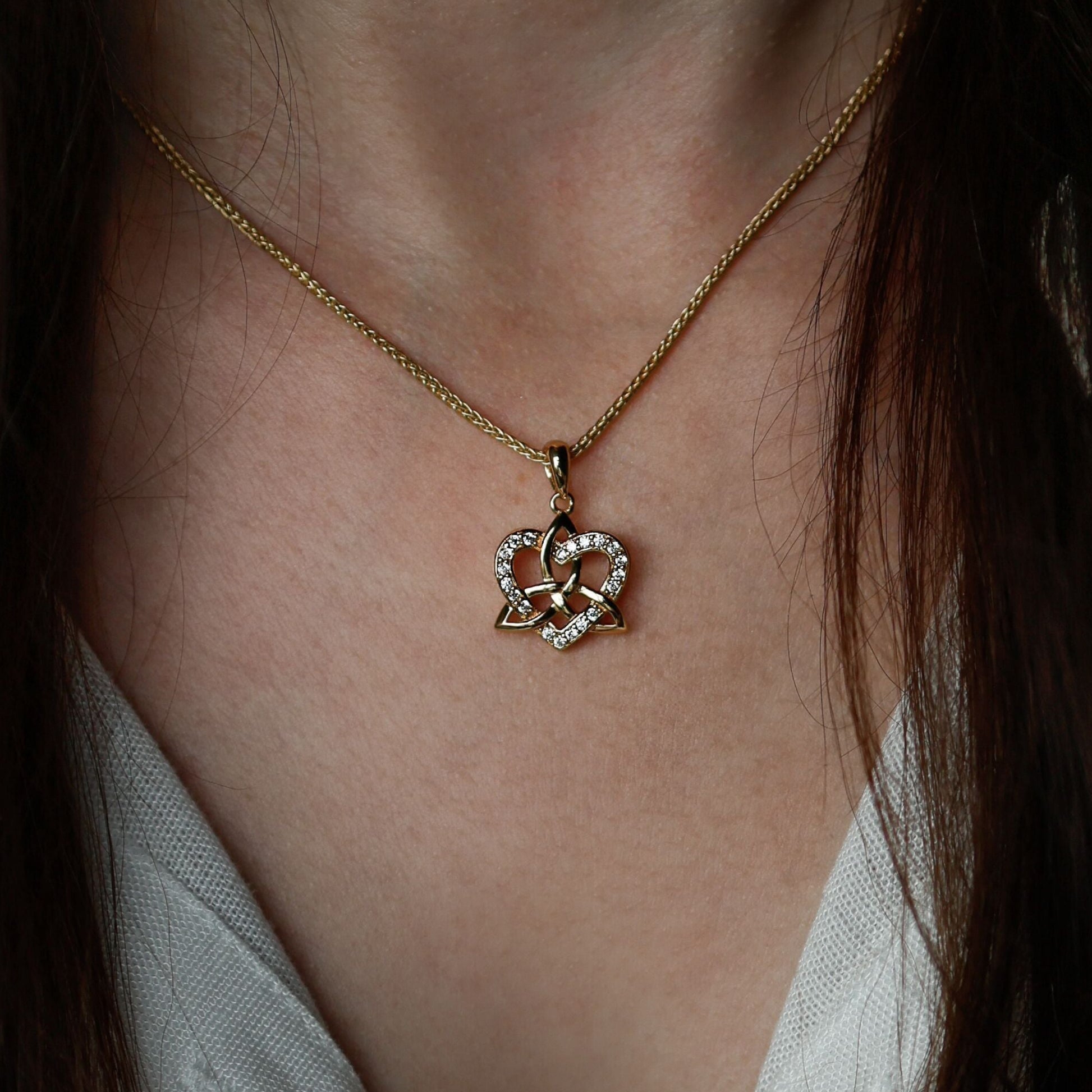 Close-up of a woman wearing a golden necklace with a heart and trinity knot pendant.