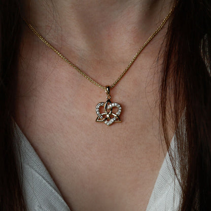 Close-up of a woman wearing a golden necklace with a heart and trinity knot pendant.