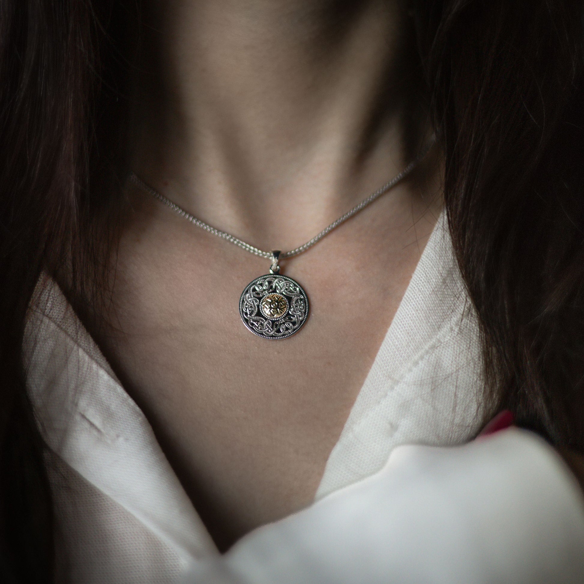 Close-up of a woman wearing a circular silver pendant with a golden center and intricate engravings.