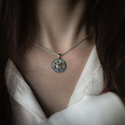Close-up of a woman wearing a circular silver pendant with a golden center and intricate engravings.