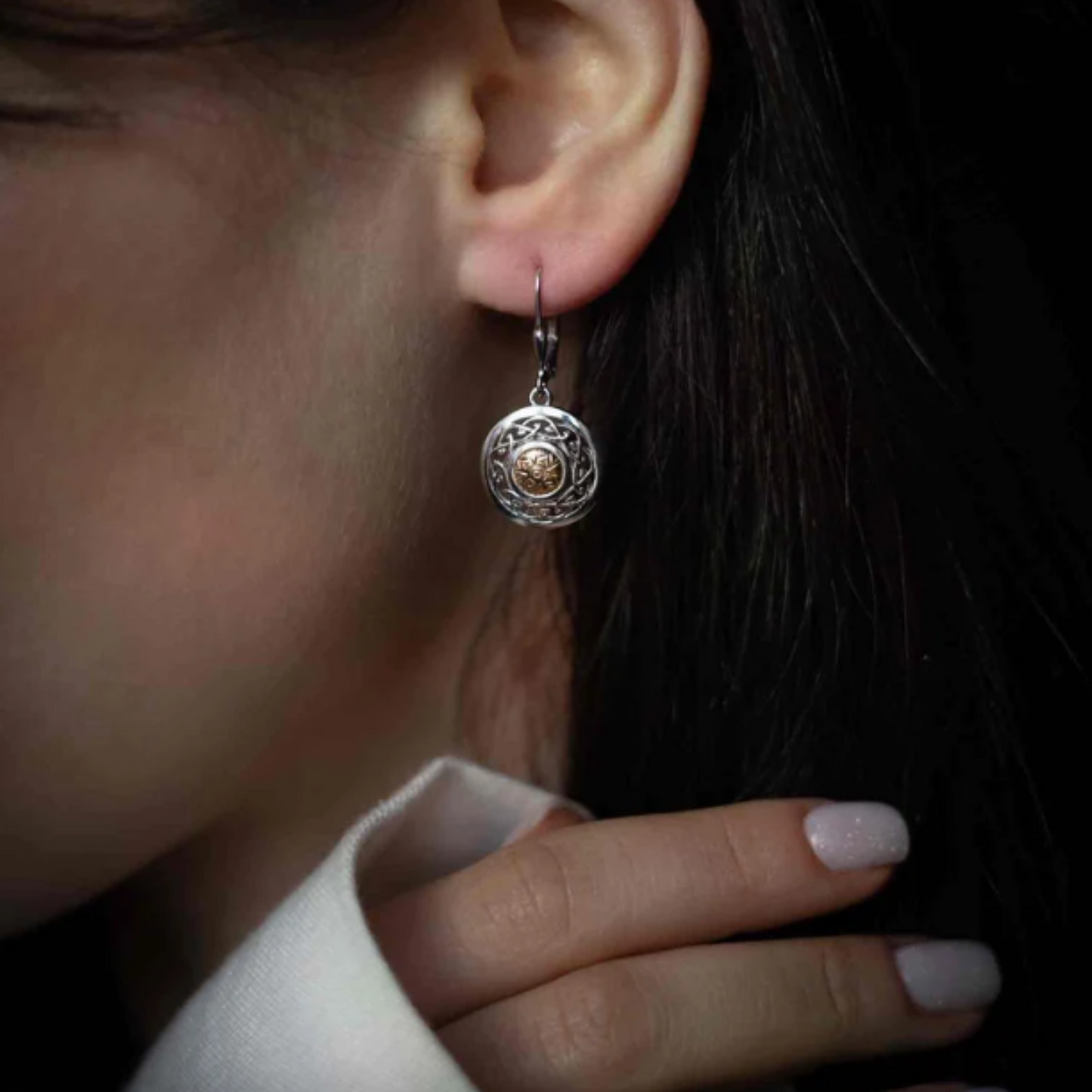 Close-up of a woman wearing a shield-shaped silver drop earring with a gold bead in the center.