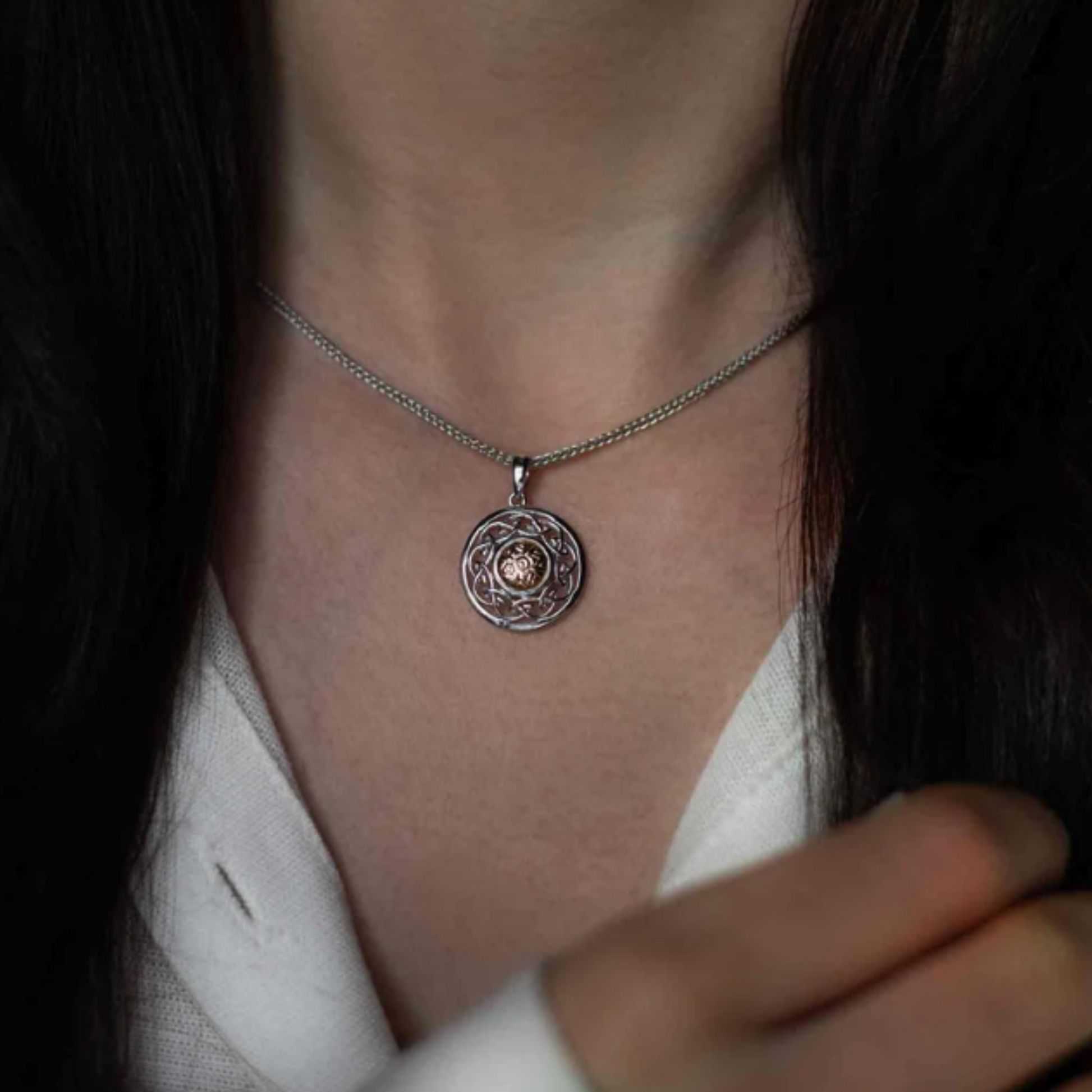 Close-up of a woman wearing a silver necklace with a shield-shaped pendant.