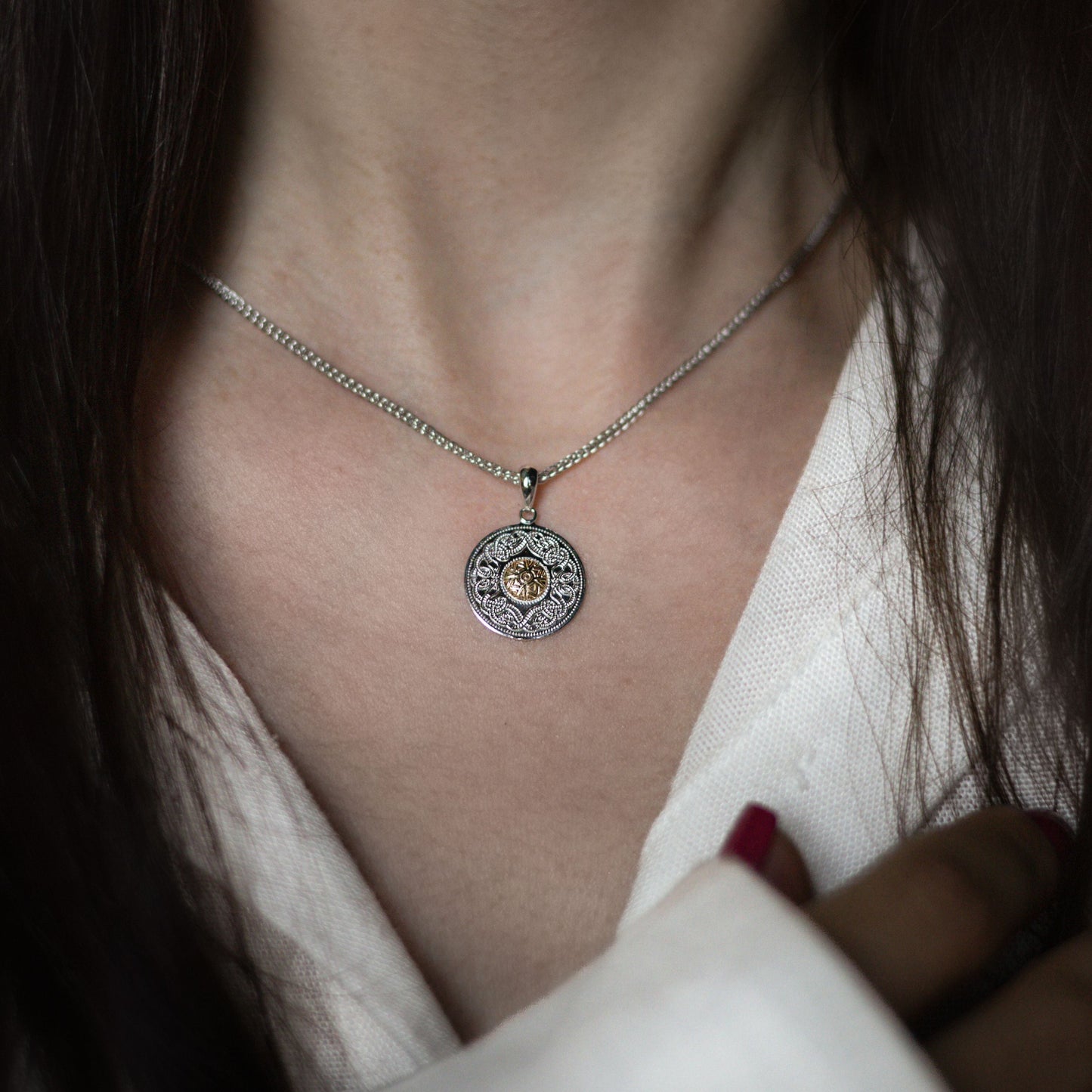 Close-up of a woman wearing a circular silver pendant with a golden center and intricate engravings.