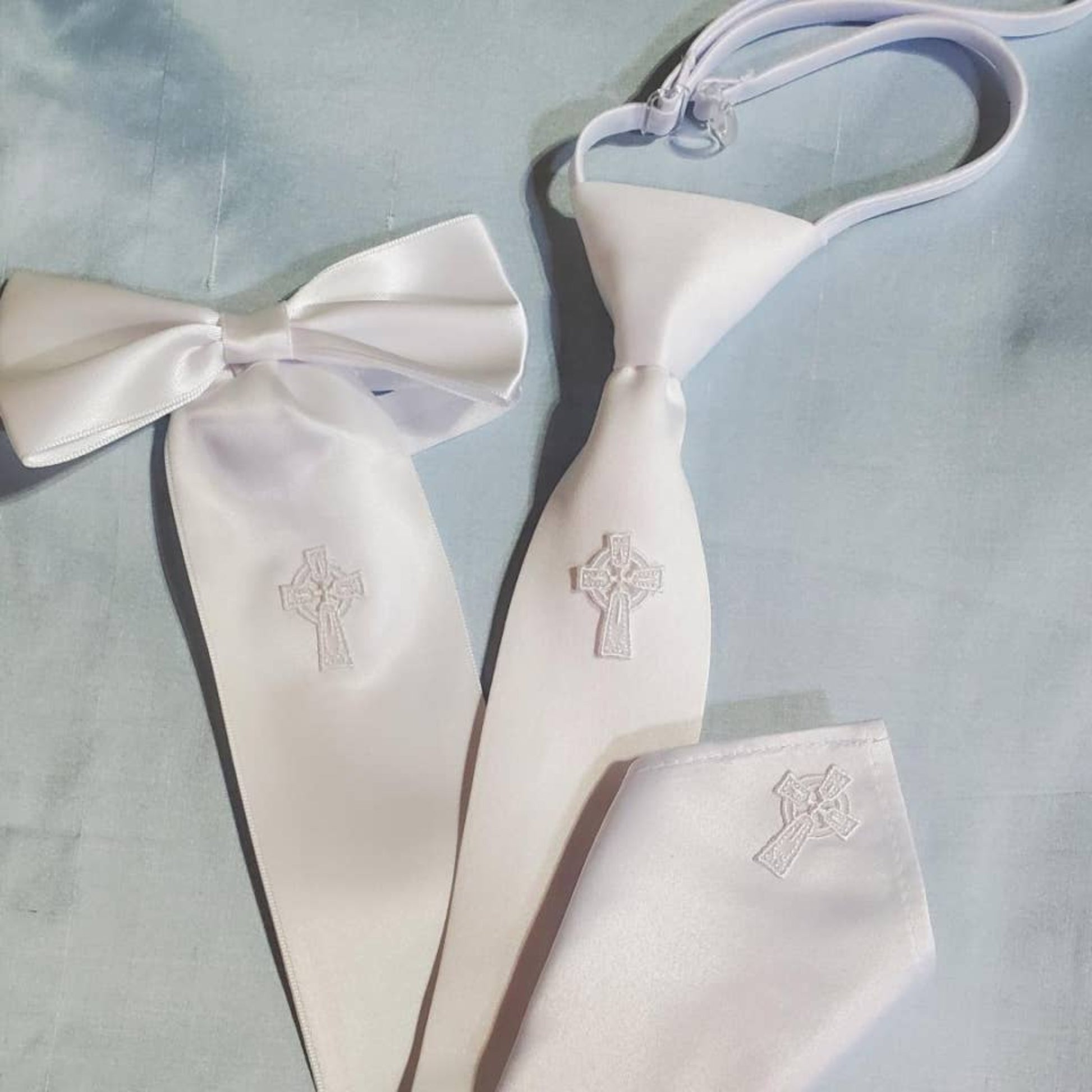 White satin bow tie and pocket square with embroidered crosses on a light blue background