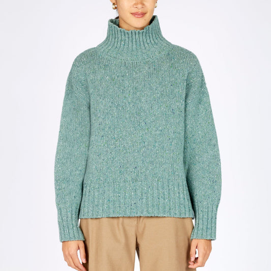 Person wearing a green sweater and beige pants on a white background