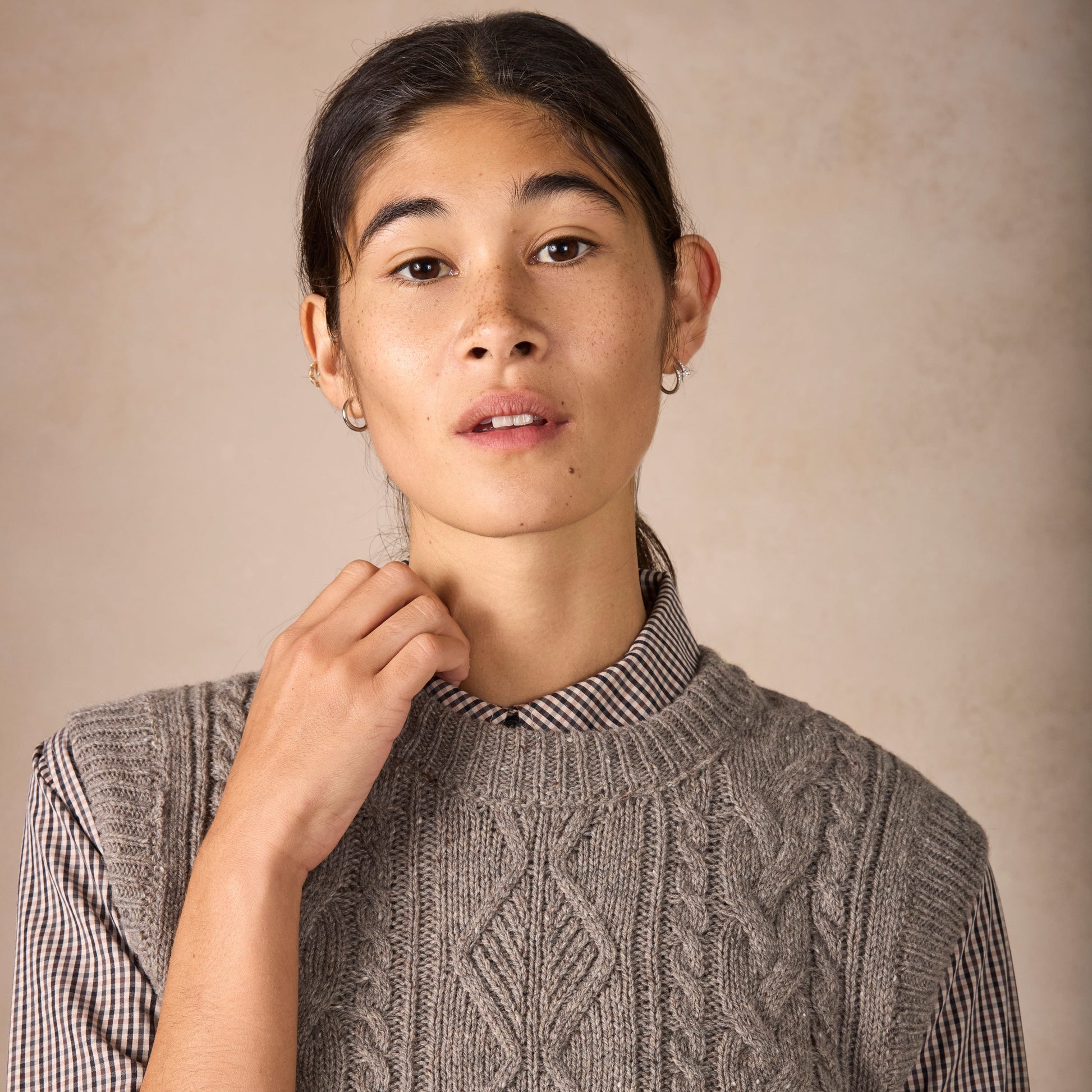 Person wearing a cable knit sweater with a plain background