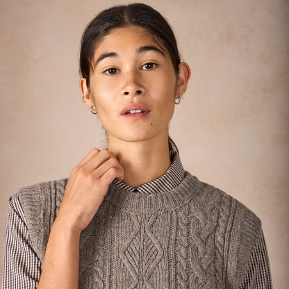 Person wearing a cable knit sweater with a plain background