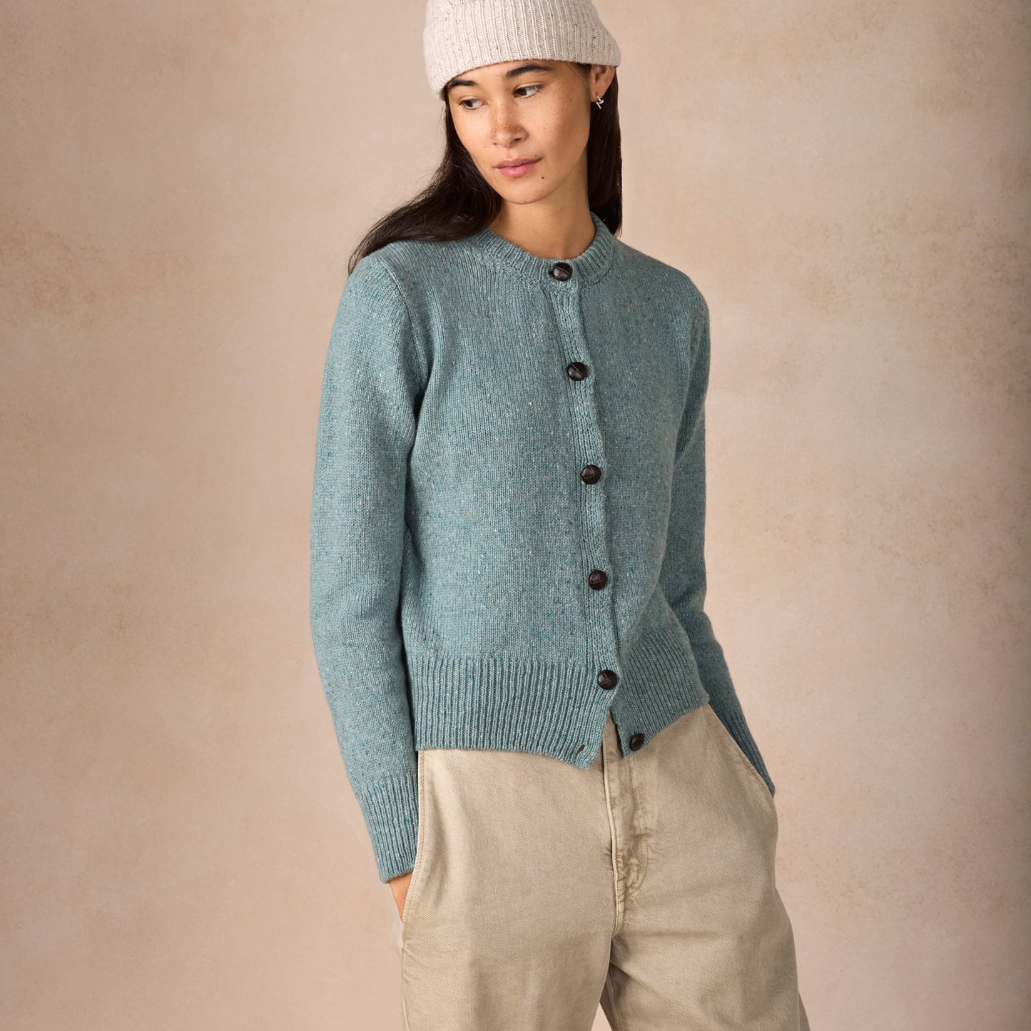 Woman wearing a light blue knitted cardigan and beige pants against a beige background