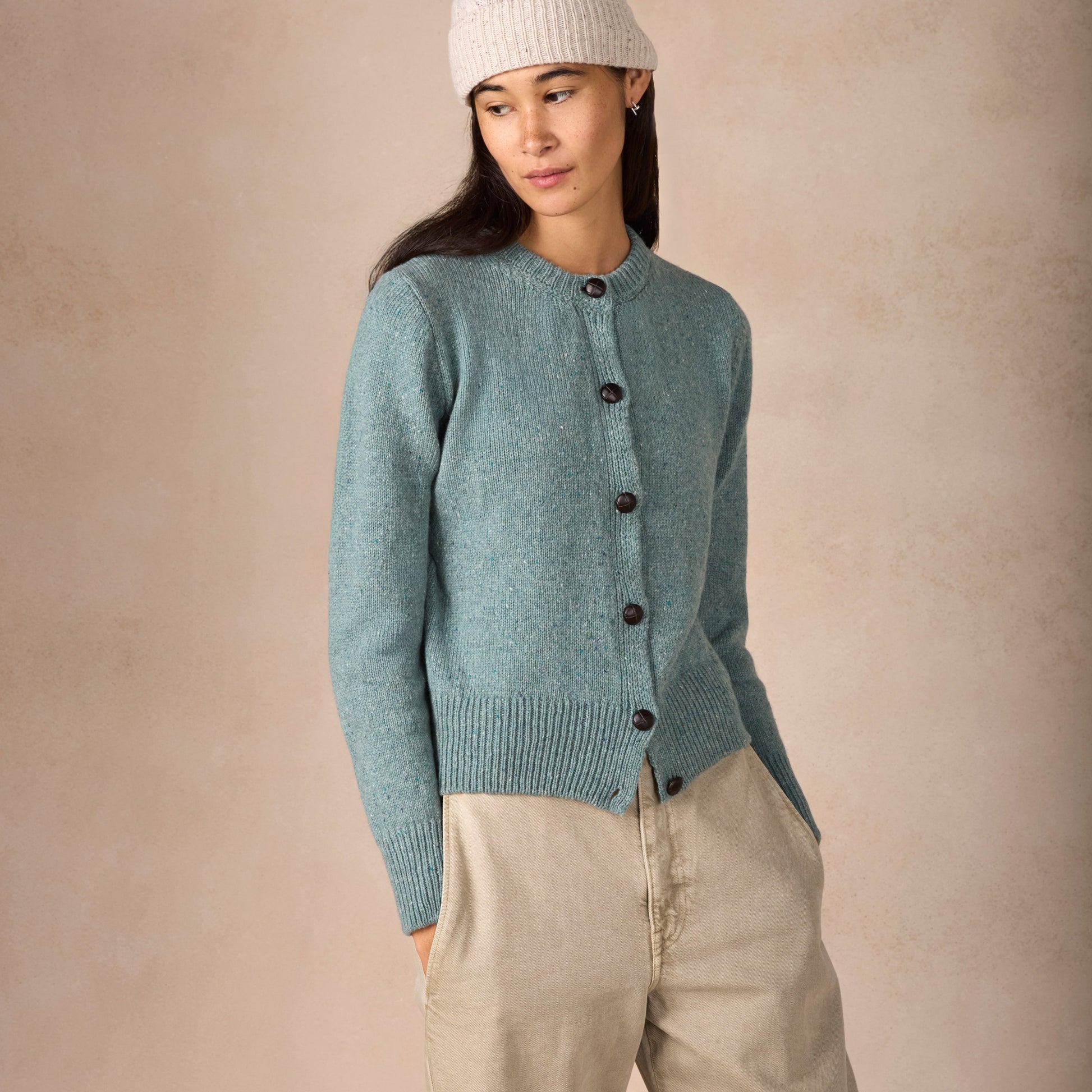 Woman wearing a light blue knitted cardigan and beige pants against a beige background