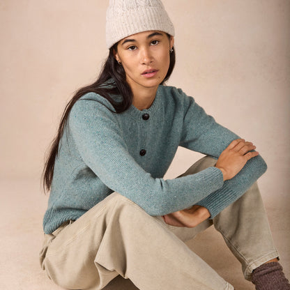 Woman wearing a light blue sweater and white knit hat sitting on a beige surface.