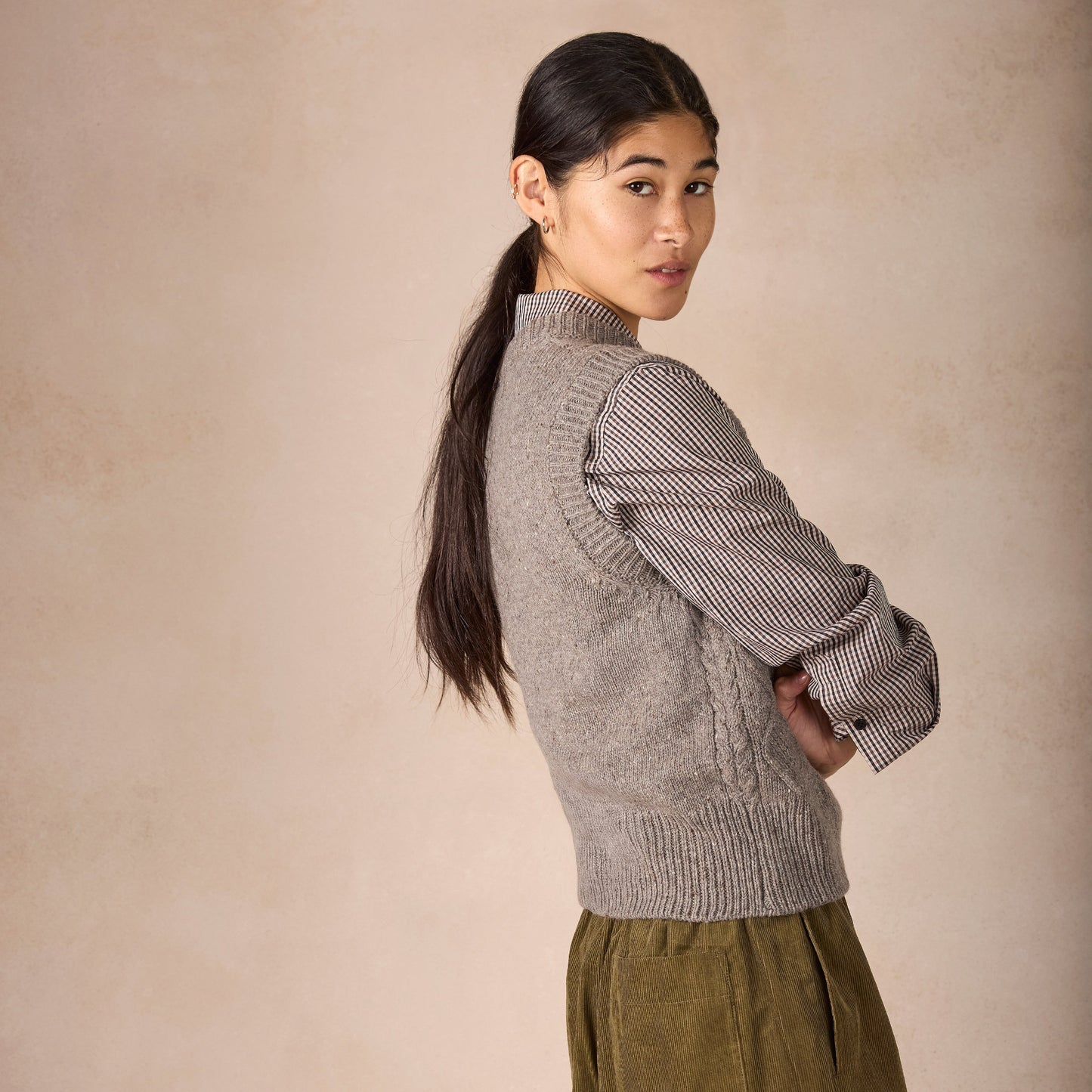 Woman wearing a gray knitted sweater and green pants against a beige background
