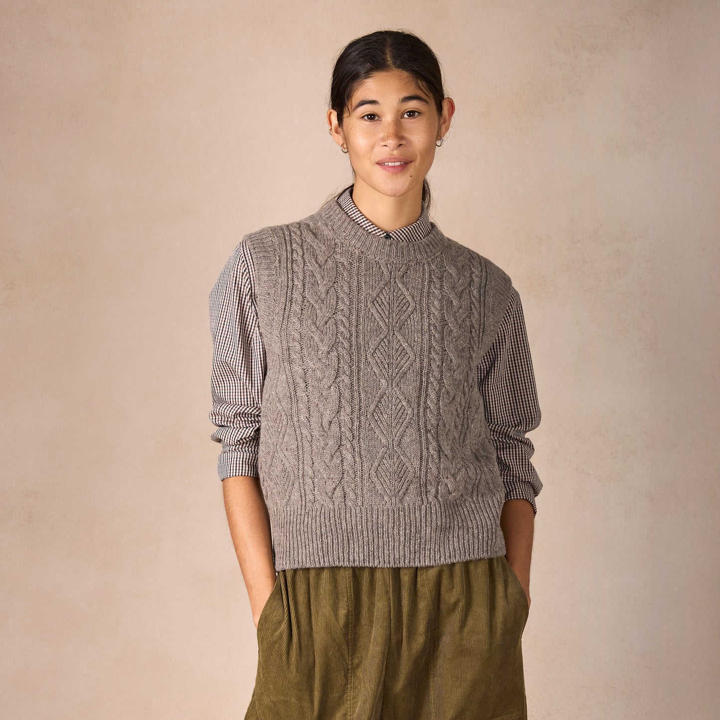 Person wearing a cable knit sweater and green pants against a beige background
