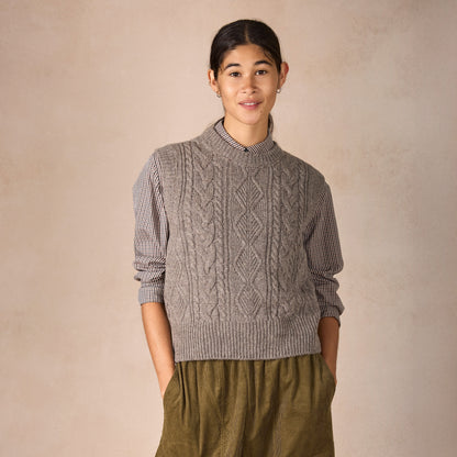 Person wearing a cable knit sweater and green pants against a beige background