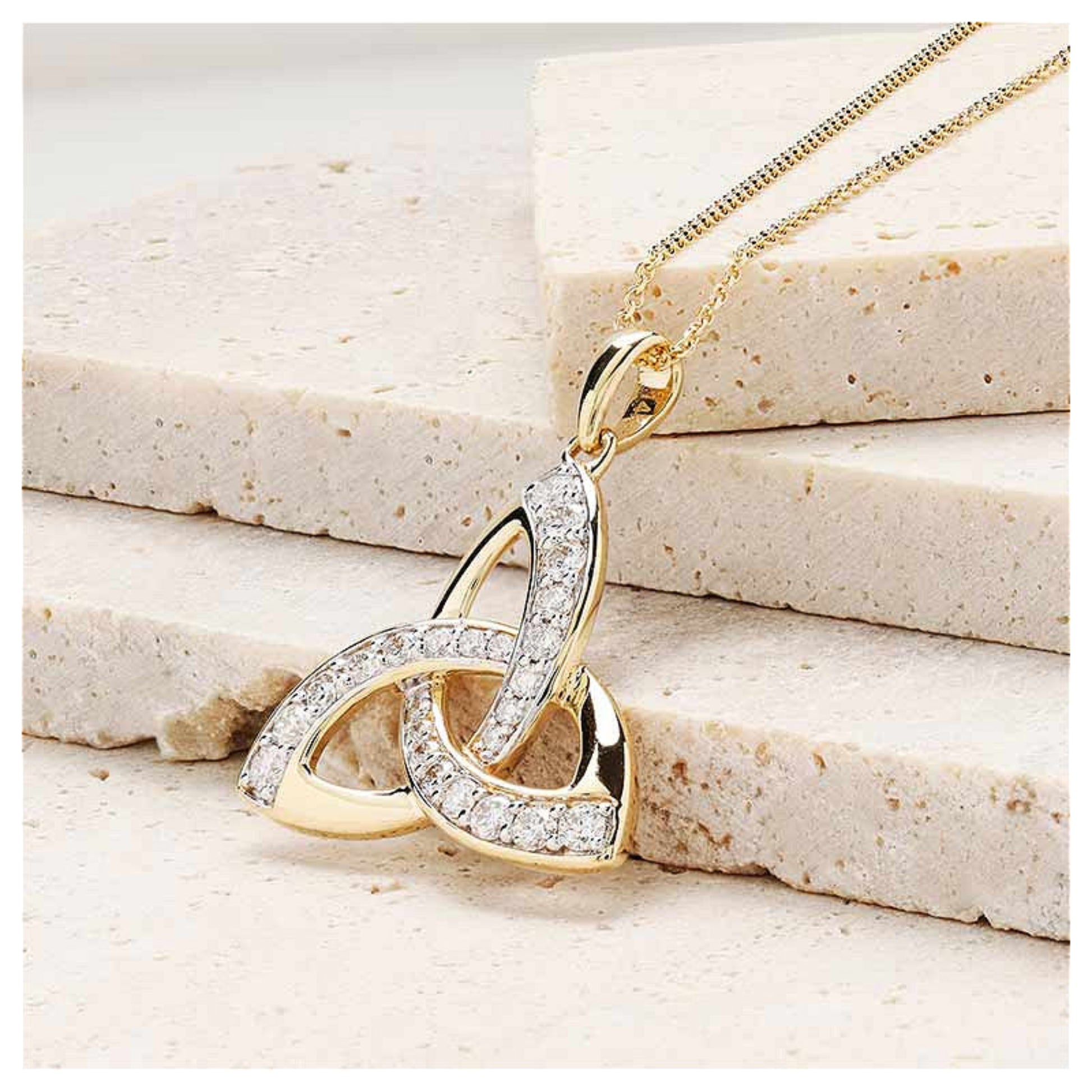 Gold trinity knot necklace resting on a marble surface