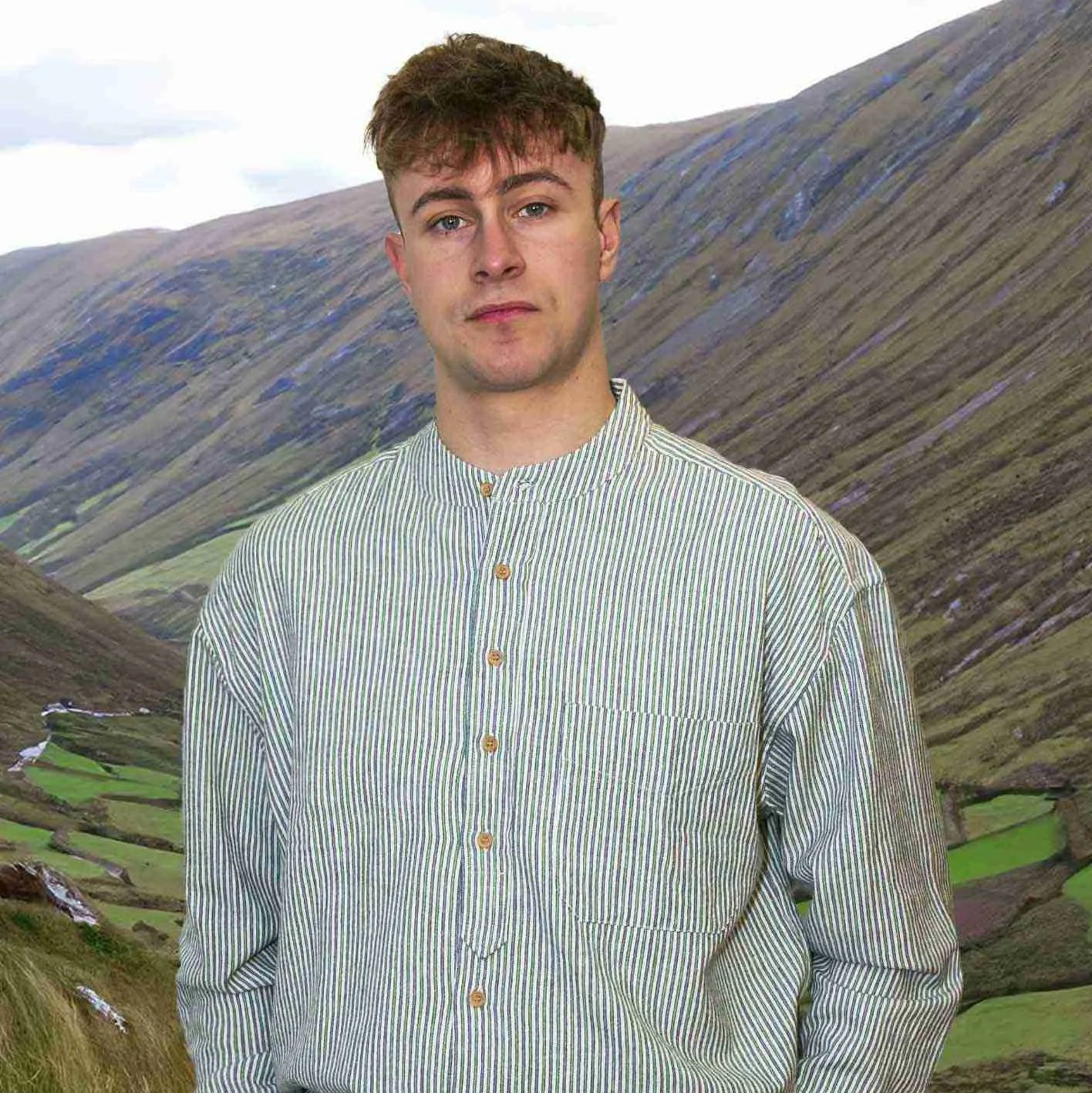 A man standing outdoors wearing a long-sleeved, button-front, striped shirt with a banded collar. The shirt is primarily green with a geometric pattern.