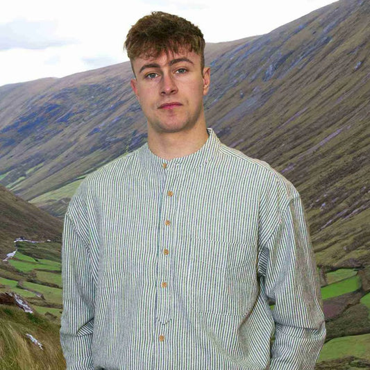 A man standing outdoors wearing a long-sleeved, button-front, striped shirt with a banded collar. The shirt is primarily green with a geometric pattern.