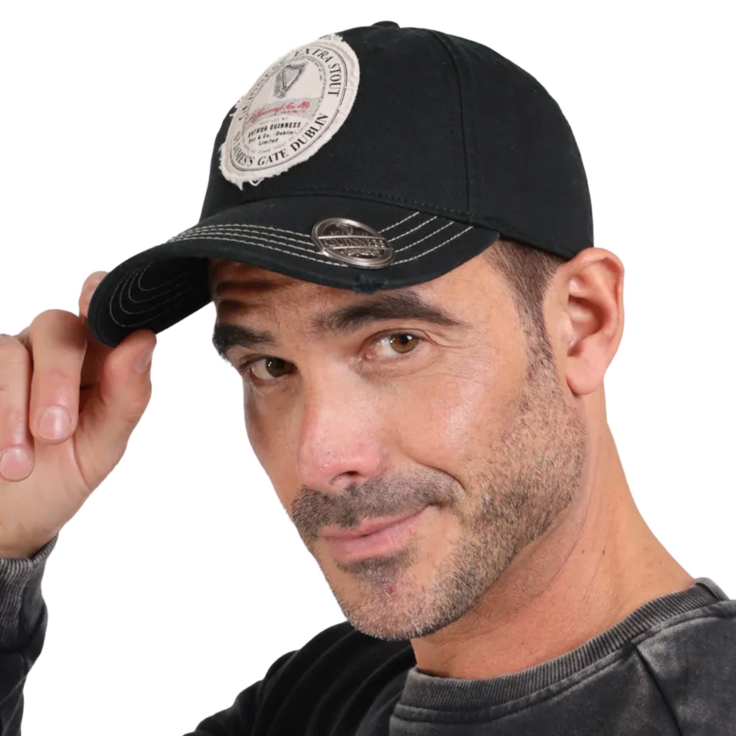 A man wearing a black baseball cap with a round guinness patch and a bottle opener on the peak.