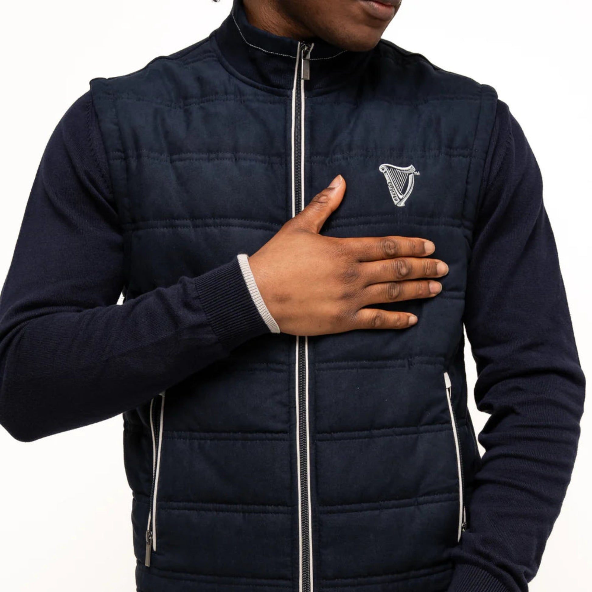Close-up of a man holding his hand against his navy quilted vest.