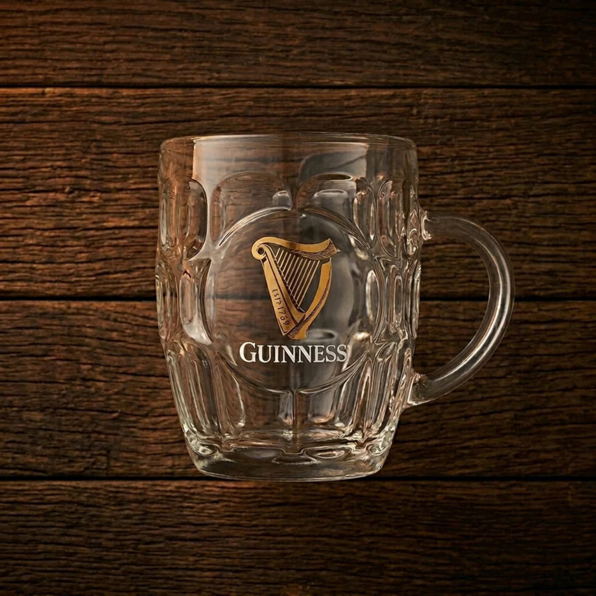 Clear Guinness mug with gold harp logo on a wooden background