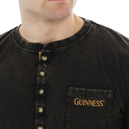 Close-up of a man wearing a long sleeve black Henley t-shirt with "guinness" written on the chest pocket.